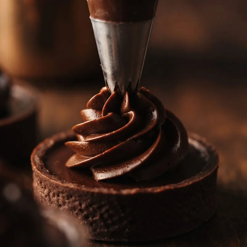 Ganache-Rosette wird mit dem Spritzbeutel auf ein Törtchen gesetzt